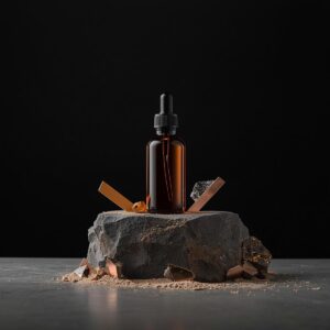 Frasco de vidro âmbar sobre uma pedra de pedreira bruta, cercado por pequenos pedaços de pirita e elementos de cobre, transmitindo solidez e equilíbrio.